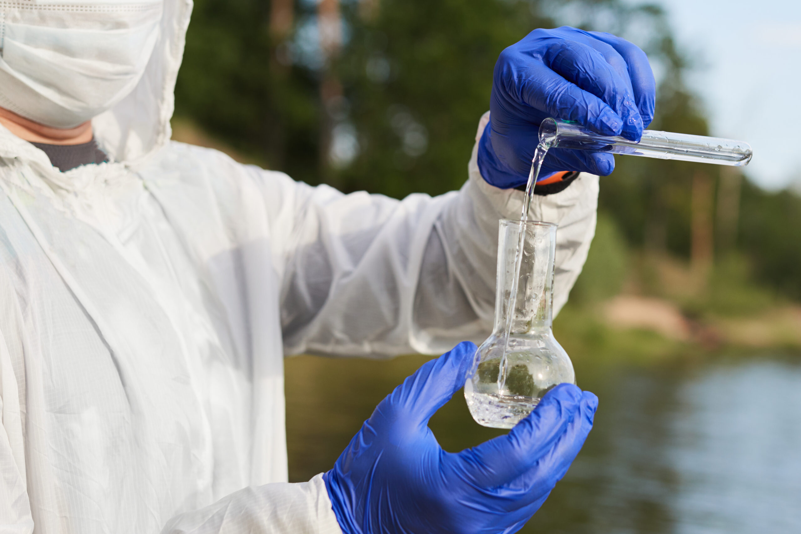 Water Purity Test. Hand holding a chemical flask or test tube with water. Lake or river in the background.